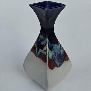 May include: A ceramic vase with a unique shape and color scheme. The top is a deep navy blue, transitioning to a blend of blue, green, and maroon. The base is a soft white, creating a striking contrast. This decorative vase is ideal for home decor.
