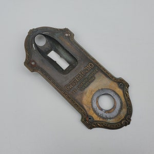 May include: A brass door knob with a keyhole and a decorative border. The knob has the text "Graybar 310" and "See License Notice on Bottom" engraved on it.