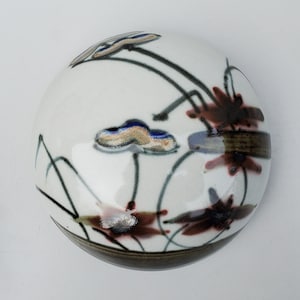 May include: A white ceramic round bowl with a brown rim and abstract floral design in shades of blue, brown, red, and gold.