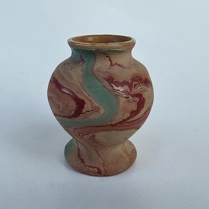 May include: A small ceramic vase with a rounded body and a flared base, featuring a marbled pattern of earthy tan, deep red, and muted sage green swirls throughout the surface, finished with a smooth texture and a wide, open circular rim.