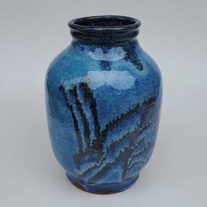 May include: A handmade ceramic vase with a rounded body and a dark blue rim. The vase is primarily a vibrant blue with black, wave-like patterns. The vase is a decorative item, suitable for displaying flowers or as a standalone art piece.
