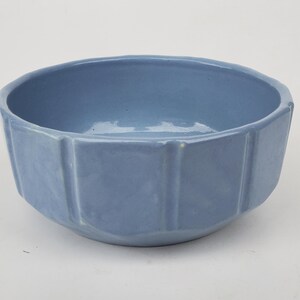 May include: A light blue ceramic bowl with a faceted exterior. The bowl has a round opening and a geometric design on the sides. The bowl is likely used for serving food or as a decorative item.