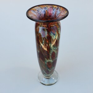 May include: A brown and green glass vase with a wide, flared opening and a clear glass base. The vase has a mottled, marbled pattern.