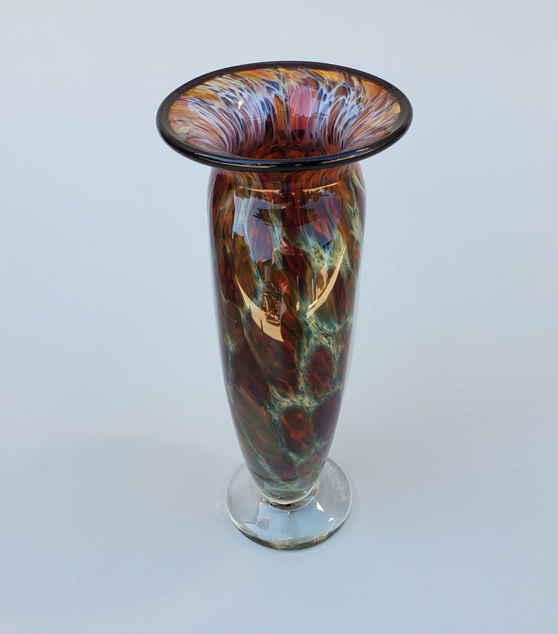 May include: A brown and green glass vase with a wide, flared opening and a clear glass base. The vase has a mottled, marbled pattern.