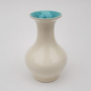 May include: A white ceramic vase with a light blue rim. The vase has a rounded body and a narrow neck.