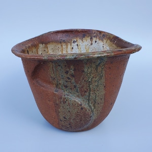 May include: A brown ceramic bowl with a white and green glaze. The bowl has a unique, organic shape and a textured surface.