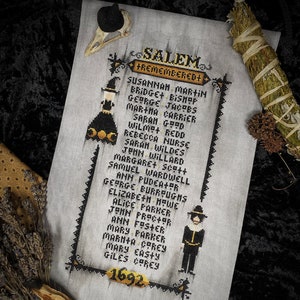 May include: A cross-stitch pattern featuring a list of names of people accused of witchcraft in Salem, Massachusetts in 1692. The names are written in black text on a white background. The pattern also includes a black and white illustration of a witch and a pilgrim.