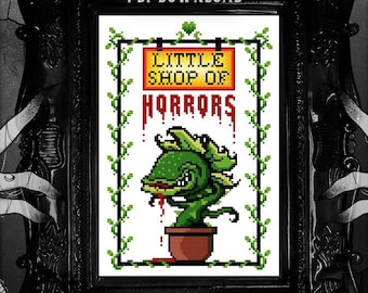 Könnte beinhalten: Ein Schwarzweißbild eines gerahmten Kreuzstich-Musters mit einer grünen Pflanze mit rotem Mund und dem Text "Little Shop of Horrors". Der Rahmen ist von zwei Händen mit schwarzen und weißen Tattoos umgeben.