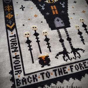 May include: Black and white cross stitch pattern featuring a witch's house with a single eye, standing on long legs. The house is surrounded by tall, thin stalks with white flowers. The text "Back to the Forest" is stitched below the house. The text "The Witchy Stitcher" is stitched below the text.