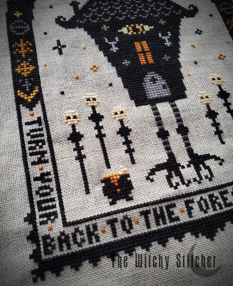 May include: Black and white cross stitch pattern featuring a witch's house with a single eye, standing on long legs. The house is surrounded by tall, thin stalks with white flowers. The text "Back to the Forest" is stitched below the house. The text "The Witchy Stitcher" is stitched below the text.