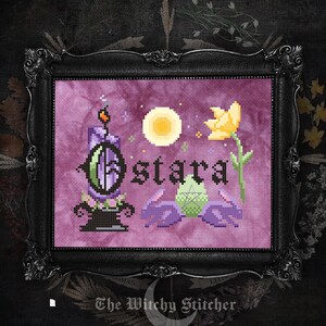 May include: A cross-stitch embroidery in a black ornate frame featuring the text Ostara in black letters. The design includes a purple candle, a yellow flower, a pale green egg with a pentagram, and two purple rabbits against a purple background.