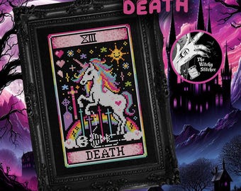 May include: A framed cross-stitch art piece featuring a white unicorn with a rainbow mane and tail, standing over a skeleton. The design includes a rainbow, stars, hearts, and crosses on a black background, with the text XIII and DEATH.