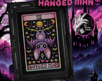 May include: A cross-stitch pattern titled HANGED MAN featuring a purple bat hanging upside down on a black background. The design includes a yellow smiley face, stars, moons, and hearts in pink, teal, and yellow. It is displayed in a black frame.