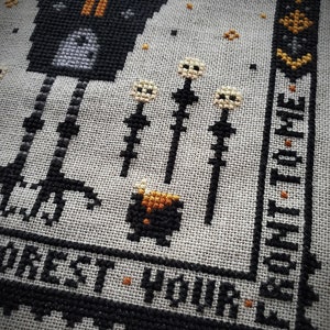 May include: Black and white cross-stitch embroidery of a witch with a cauldron and the text "Forest Your Time".