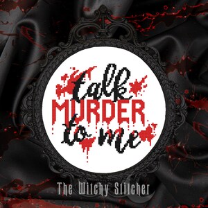 May include: A white cross-stitch embroidery hoop with black lettering that reads "Talk Murder to Me" with red blood splatter accents. The hoop is framed in a black metal frame. The text "The Witchy Stitcher" is below the hoop.