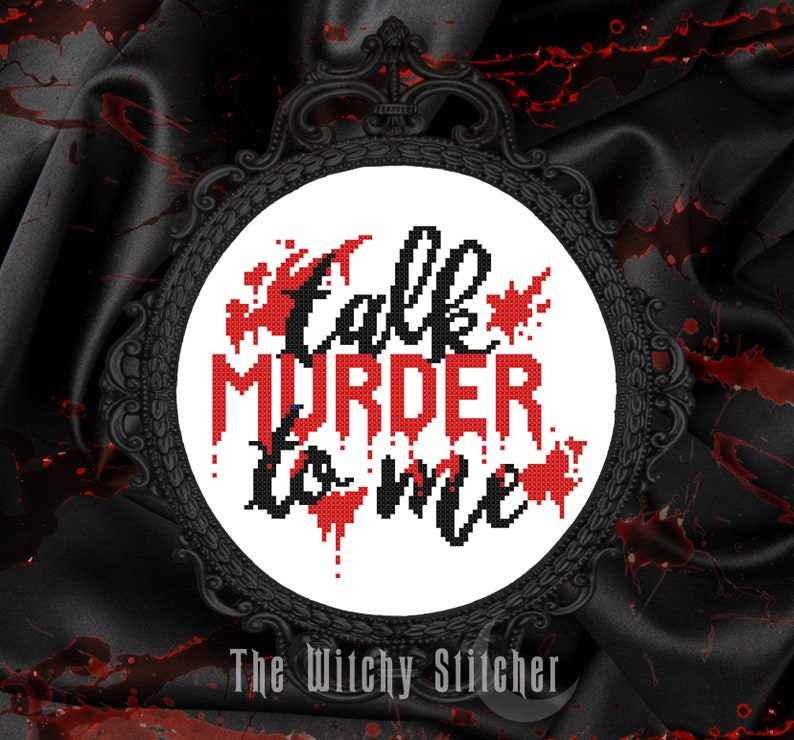 May include: A white cross-stitch embroidery hoop with black lettering that reads "Talk Murder to Me" with red blood splatter accents. The hoop is framed in a black metal frame. The text "The Witchy Stitcher" is below the hoop.