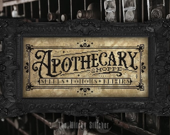 May include: A rectangular cross-stitch embroidery in a black ornate frame featuring the text Apothecary Shoppe, Spells + Potions + Elixirs in black thread on a mottled tan fabric background with decorative borders and small cross motifs.