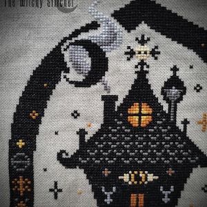 May include: Cross stitch pattern of a black and gray haunted house with orange windows and a crescent moon in the background. The text "The Wilky Stitcher" is in the top left corner.