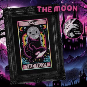 May include: Framed cross-stitch art featuring a tarot card design. The card shows a smiling moon above a whale, with a rainbow and the text "THE MOON". The frame is black, with a gothic castle background.