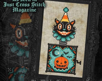 May include: A cross-stitch pattern featuring a black cat jack-in-the-box with a party hat and teal ruff, emerging from a box decorated with a pumpkin, moon, and bats. The text reads As seen in Just Cross Stitch Magazine and The Witchy Stitcher.