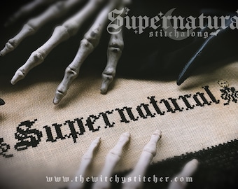 May include: Cross stitch pattern of the word "Supernatural" in black thread on beige Aida cloth.  The pattern is surrounded by skeletal hands.