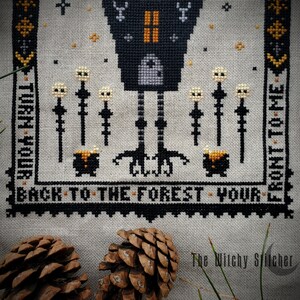 May include: Cross-stitch pattern featuring a black crow with a house on its back, standing on a forest path with a cauldron and mushrooms. The text reads "Turn your back to the forest - your front to me."