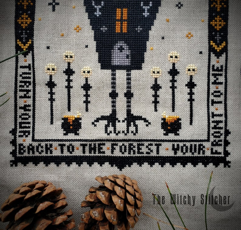 May include: Cross-stitch pattern featuring a black crow with a house on its back, standing on a forest path with a cauldron and mushrooms. The text reads "Turn your back to the forest - your front to me."