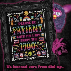 May include: A framed cross-stitch with the text "PLEASE BE PATIENT WITH ME I AM FROM THE 1990'S". The design includes a rainbow, cassette tape, and other 90s-themed icons. A purple Furby peeks from behind the frame.