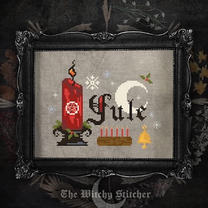 May include: A cross-stitch embroidery piece in a black ornate frame featuring a red candle with a pentacle, the text Yule, a white crescent moon, a brown log with six small red candles, a gold bell, and white snowflakes on a grey fabric background.