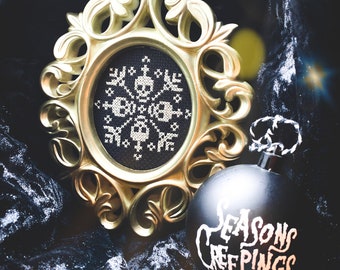May include: A black and white cross-stitch design of a skull and crossbones in a gold ornate frame. A black Christmas ornament with the text "Seasons Creepings" is next to the frame.