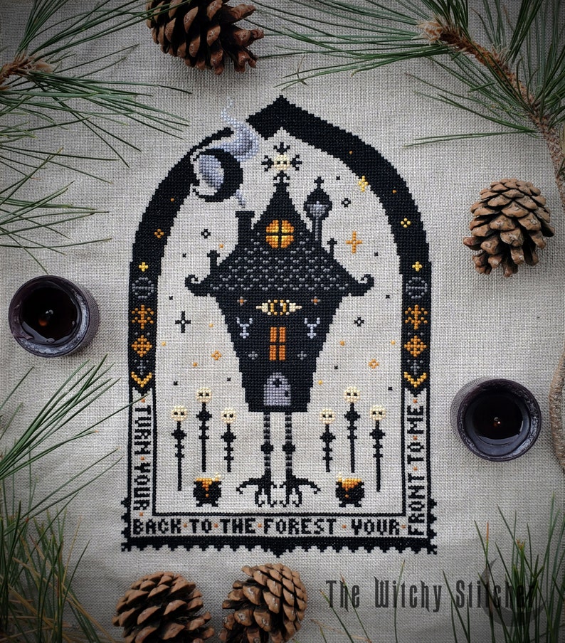 May include: Black and white cross stitch pattern of a spooky house with a moon and stars. The house is on stilts and has a cauldron and skeletal figures. The text reads "Turn your back to the forest, your front to me."
