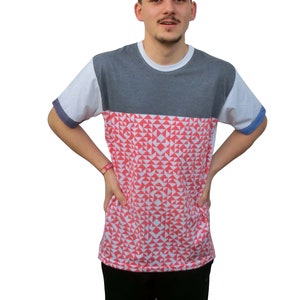 May include: A short-sleeve crew neck t-shirt featuring a dark gray upper chest panel, white sleeves with blue trim, and a lower section patterned with a repeating geometric design of small white and coral-colored triangles and semi-circles.