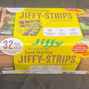 May include: A stack of three brown Jiffy-Strips seed starting trays, each with 32 peat cells. The packaging shows a yellow background with the text "Seed Starting Jiffy-Strips 32 Organic Peat Cells" and a picture of seedlings growing in the trays.