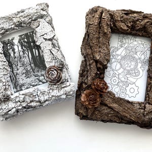 May include: Two rustic picture frames with bark-like textures. One is painted silver and the other is brown. Each frame has a small pinecone embellishment. The frames hold black and white images.