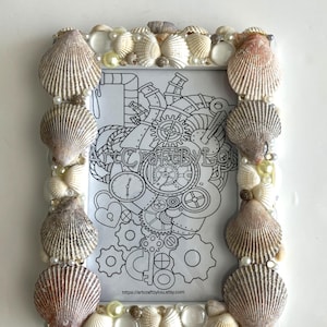 May include: White picture frame decorated with seashells and pearls. The frame contains a black and white illustration of a steampunk heart with gears and a key. The text "ArtCraftByLou" and "https://artcraftbyyou.etsy.com" are visible at the bottom of the image.