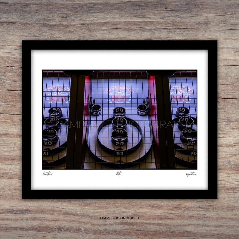 May include: A framed print of a vintage Skee-Ball game. The game features a series of numbered targets and a ramp for rolling balls. The print includes the text "FRAMES NOT INCLUDED".
