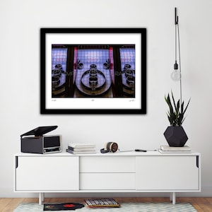 May include: A framed photograph of a skee-ball machine with a black frame. The machine has a series of circular targets with point values. The background is a grid of lights. The photograph is displayed on a white cabinet with a record player and a plant.