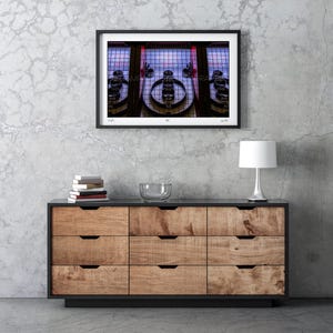 May include: A framed photograph of a vintage Skee-Ball machine. The image is in a black frame and hangs above a wooden dresser. The Skee-Ball machine has a series of numbered targets and a red and blue color scheme.