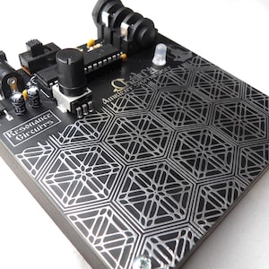 Peut inclure: Circuit imprimé électronique noir avec un motif géométrique argenté et le texte "Resonance Circuits" et "Chakra Ambient Synthesizer". Comprend des boutons, des prises et d'autres composants électroniques.