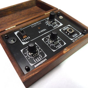 May include: A wooden box with a hinged lid, housing a black panel with white text and dials. The panel features the text "BRANTON", "SIGNAL", "LEVEL", "FREQ", "SWEEP", "SCAN", "POWER", and "ResonanceCircuits". The box is stained a dark brown.