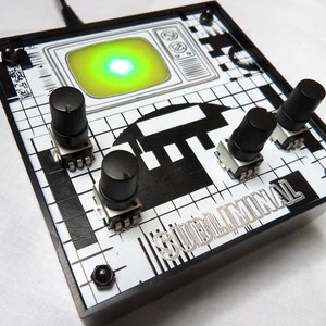 May include: A black box with a white and black grid pattern and the text "Subliminal" printed on the bottom. The box has three black knobs and a small green screen with a white light in the center.