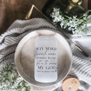 May include: A white glass tumbler with the words "WAY MAKER, miracle worker, promise keeper, light in the darkness, MY GOD, THAT IS WHO YOU ARE" printed in black. The tumbler sits on a white plate, with a candle and flowers in the background.