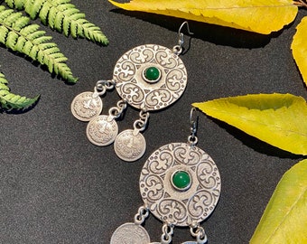 Può includere: Orecchini d'argento con un designo circolare e una pietra verde al centro. Gli orecchini hanno tre piccoli ciondoli circolari che pendono dalla parte inferiore.