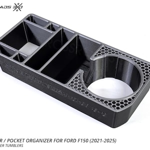 May include: A black cup holder and pocket organiser for a Ford F150 truck. The organiser has multiple compartments and a cup holder with a honeycomb design. The text "CROSSROADS" is visible on the side. The product fits Yeti and other tumblers.