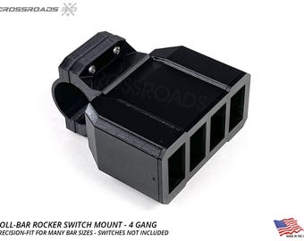 May include: Black roll-bar rocker switch mount with four rectangular openings. The mount is designed to fit various bar sizes. The text "ROLL-BAR ROCKER SWITCH MOUNT - 4 GANG" is visible. Made in the USA.