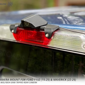 以下が含まれることがあります： 青いフォードF150トラックに取り付けられた黒いWolfboxカメラマウント。マウントは赤いブレーキライトの上に配置され、「WOLFBOX CAMERA MOUNT FOR FORD F150 (15-25) & MAVERICK (22-25)」というテキストが含まれています。