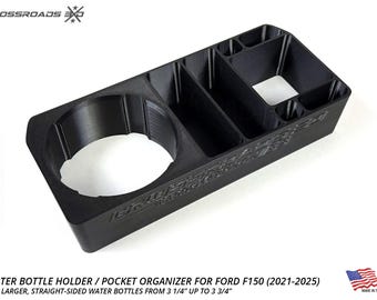 May include: Black plastic water bottle holder and pocket organizer for Ford F150 trucks. Features a large circular opening for a water bottle and several smaller compartments. Fits water bottles from 3 1/4" to 3 3/4".