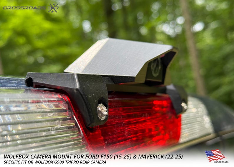 以下が含まれることがあります： Ford F150 (15-25) および Maverick (22-25) 車両用の黒い Wolfbox カメラマウント。マウントは銀色のトップです。画像には赤いテールライトと「MADE IN THE USA」の文字も表示されています。