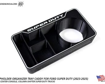 Op de afbeelding: Zwarte bekerhouder organizer tray caddy voor Ford Super Duty trucks. Voorzien van een bekerhouder en meerdere compartimenten. De tekst "SUPER DUTY" is in het wit weergegeven. Gemaakt in de VS.