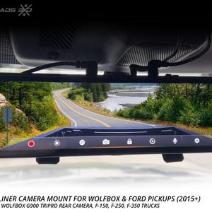 May include: A black rear view mirror with a built-in camera displaying a scenic road view. The mirror has a touch screen with icons and is mounted on a vehicle's windshield. Text at the bottom reads "REAR HEADLINER CAMERA MOUNT" and "MADE IN THE USA."